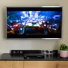 A television set is mounted on a wall above a black media console. On the console, a soundbar and a DVB-T2 receiver are placed. A small potted plant sits to the right of the receiver. Voir les images du produit
