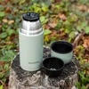 A light green thermos bottle and two cups are placed on a tree stump outdoors, surrounded by foliage. Voir les images du produit
