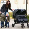 A woman pushing a double stroller with two young children in it, outdoors. Produktbild-Vorschau