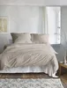 A neatly made bed with beige bedding in a room with white walls and a window. Produktbild-Vorschau