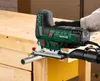 A person is using a jigsaw to cut a metal pipe attached to a wooden workbench. Produktbild-Vorschau