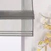 A close-up view of a gray sheer Roman blind with horizontal stripes, partially covering a window. A decorative branch with white and yellow leaves is visible to the right. Produktbild-Vorschau