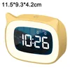 A yellow digital alarm clock with a cat-ear design, displaying the time 10:26 AM and two alarm icons. The clock has a soft, glowing light around its screen. Produktbild-Vorschau