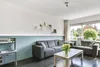 A living room with two sofas, a coffee table with flowers, and a large window overlooking a garden. Produktbild-Vorschau