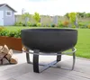 A black metal fire pit on a wooden deck in a backyard setting, with a small shed and greenery in the background. Produktbild-Vorschau