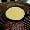 A crêpe pan with a crêpe being cooked on a grill over hot coals. Produktbild-Vorschau