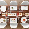 A beautifully set dining table with white plates, cutlery, and various small dishes of food. Produktbild-Vorschau