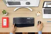 A top-down view of a desk with a computer monitor, laptop, keyboard, mouse, coffee cup, and notebook. Produktbild-Vorschau