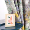A framed picture of vases and fruit sits on a dark blue tray, with floral curtains in the background. Produktbild-Vorschau