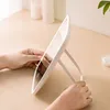 Hands holding a white LED makeup mirror on a wooden desk. Podgląd zdjęcia produktu