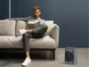 A man is sitting on a couch reading a book, with a space heater in the foreground. Voir les images du produit
