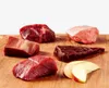 Several pieces of raw meat and apple slices are arranged on a wooden cutting board against a white background. Produktbild-Vorschau