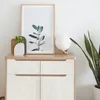 A modern cabinet with decorative items on top, including a framed plant picture, a vase, and a globe lamp. Produktbild-Vorschau