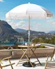 A white fringed umbrella over a bamboo table and chairs on a balcony with a scenic view of a lake and mountains. Náhľad obrázku produktu