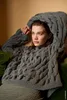 A woman wearing a chunky knit sweater is lounging on a sofa. Produktbild-Vorschau