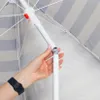 A hand is shown adjusting the pole of a striped umbrella. Náhled obrázku produktu