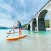 People paddleboarding on a lake under a large stone bridge. Náhľad obrázku produktu