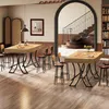 A dining area with two high tables and stools, a staircase in the background, and a bookshelf. Voir les images du produit