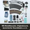 A collection of model car kit components, including car parts, track pieces, electronics, and a screwdriver, arranged on a white background. Náhľad obrázku produktu