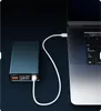 A dark blue power bank is connected to a laptop via a white USB-C cable. The power bank has a digital display showing charging information. Náhled obrázku produktu