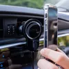 A person is holding a smartphone next to a car's air vent where a phone holder is attached. Náhled obrázku produktu
