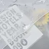 A close-up view of a white sheer curtain with a silver marble pattern, partially covering a book and some yellow flowers. Produktbild-Vorschau