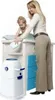 A woman is changing a baby on a changing table, with a diaper pail next to it. Produktbild-Vorschau