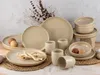A collection of beige stoneware dishes and cups arranged on a textured surface with dried plant elements in the background. Produktbild-Vorschau