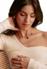 A woman wearing a cream-colored off-the-shoulder top and a necklace with charms. Anteprima dell’immagine prodotto