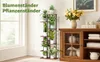 A multi-tiered wooden plant stand filled with various potted plants is placed next to a window. A wooden cabinet with glass doors is visible to the right, adorned with a vase of yellow flowers. Produktbild-Vorschau