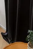 A close-up view of a black velvet curtain hanging next to a white wall, with a wooden table and a plant in the foreground. Produktbild-Vorschau