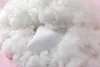 A white pillow is nestled within a large pile of fluffy white filling, likely polyester fiberfill, on a pink background. Produktbild-Vorschau
