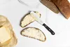 A butter knife is shown spreading butter on slices of bread, with a block of butter and loaves of bread in the background. Produktbild-Vorschau