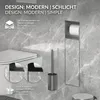 A modern bathroom setting featuring a toilet, toilet brush holder, and toilet paper holder against a marble-patterned wall. Produktbild-Vorschau