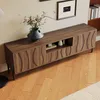 A wooden TV stand with decorative wave-like fronts is shown in a living room setting, with a vase of flowers on top and a bookshelf in the background. Anteprima dell’immagine prodotto