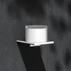 A white soap dispenser sits on a silver shelf mounted on a dark gray textured wall. Produktbild-Vorschau