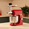 A red Kenwood stand mixer with a meat grinder attachment sits on a countertop in a kitchen. Voir les images du produit