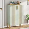 A light green shoe cabinet with gold accents and legs, placed in an entryway next to a white door. Produktbild-Vorschau