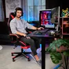 A man is sitting in a gaming chair at a desk with a computer setup. Náhled obrázku produktu