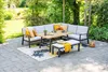 An outdoor seating area with a sectional sofa, table, and bench on a patio with a rug and plants in the background. Produktbild-Vorschau