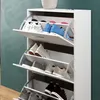A white shoe cabinet with multiple shelves, each holding pairs of shoes. The cabinet is shown in a room with a teal wall and a wooden floor. Produktbild-Vorschau