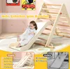 A young child is sliding down a wooden climbing structure indoors. Produktbild-Vorschau