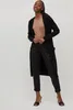 A woman is posing in a studio setting wearing a long black cardigan over a tan top and black pants. Produktbild-Vorschau
