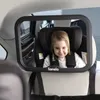A young child is sitting in a car seat, viewed through a baby car mirror. The mirror is attached to the headrest of the front seat, allowing the driver to see the child in the back seat. Produktbild-Vorschau