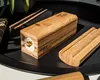 A sushi-making tool with a piece of sushi inside, placed on a black tray with chopsticks and a bamboo mat. Náhľad obrázku produktu