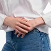 A person wearing a white shirt and blue jeans, showing off a ring and a bracelet. Voir les images du produit