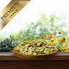 A wooden bowl filled with green flakes sits on a wooden surface, with a blurred background of greenery and flowers. Produktbild-Vorschau