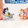 Two Bluey toy figures are shown on a white surface, with a person's hands holding them. Voir les images du produit