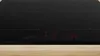 A black induction cooktop with red digital displays, set against a light gray background and a wooden surface in the foreground. Produktbild-Vorschau