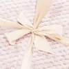 A close-up of a cream-colored ribbon tied into a bow on a textured pink surface. Náhled obrázku produktu